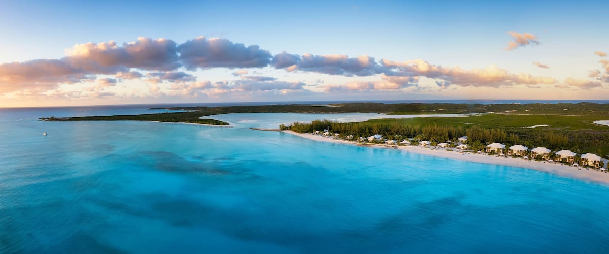 A coastal landscape with a clear blue sea, a sandy beach, and a small island with buildings.