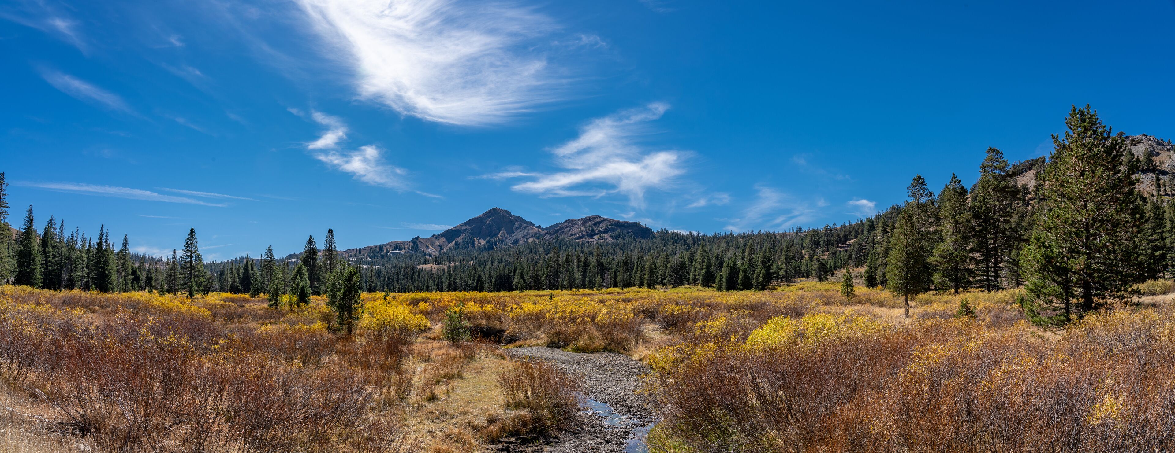 A mountainous landscape with a river, autumn-colored vegetation, and a clear blue sky.