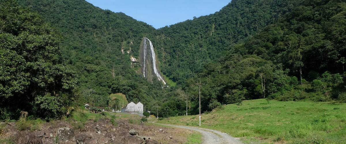 A dirt road leading to a waterfall in a forested valley.