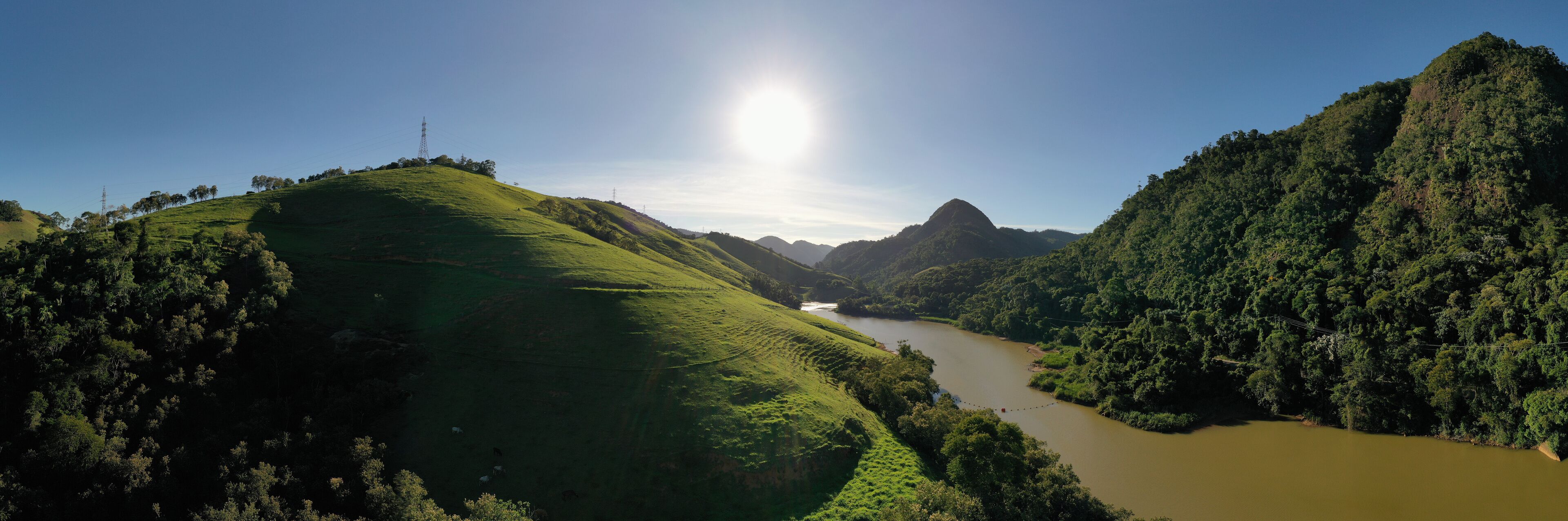 A river winding through lush green hills with a clear sky and a power line tower in the distance.