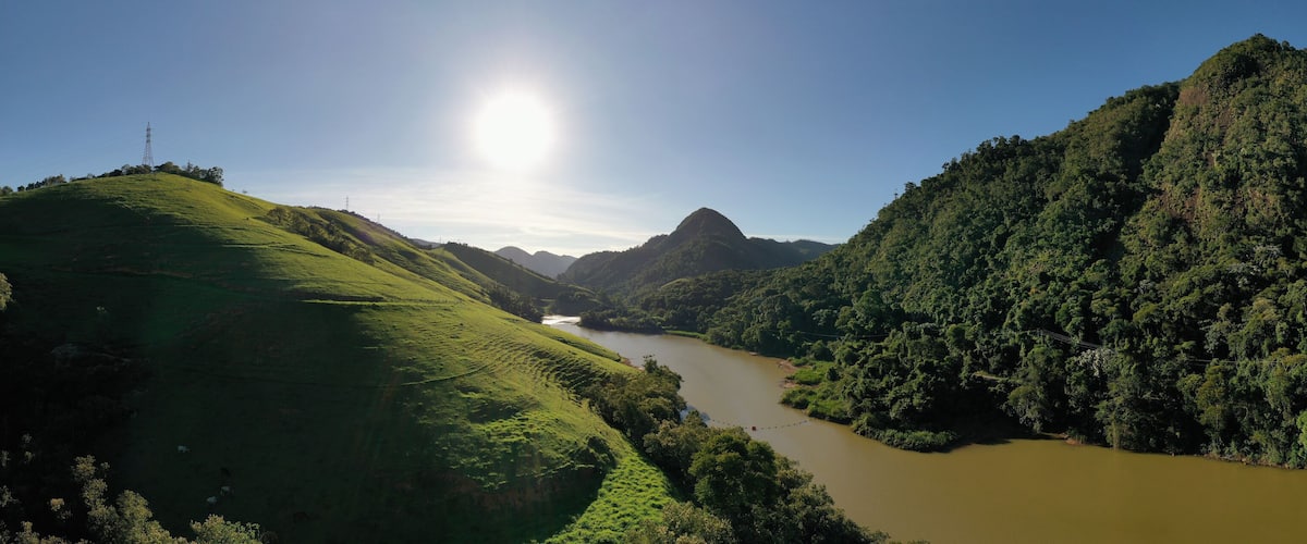A river winding through lush green hills with a clear sky and a power line tower in the distance.