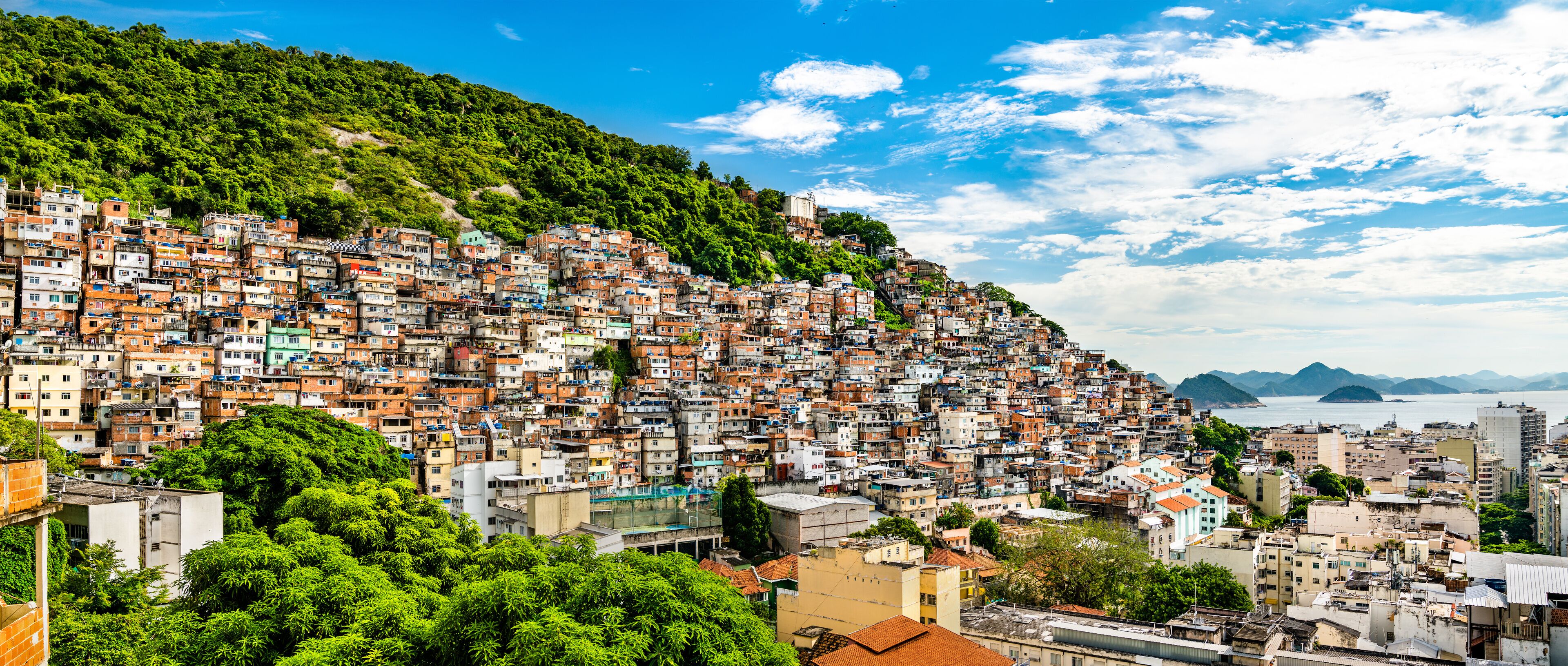 A densely packed hillside cityscape with a view of the ocean and mountains in the distance.