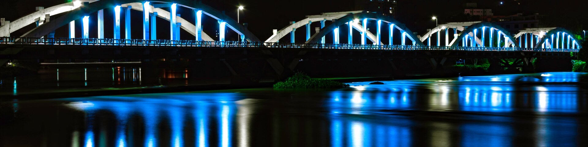 A bridge with blue lights at night, reflecting on the water.