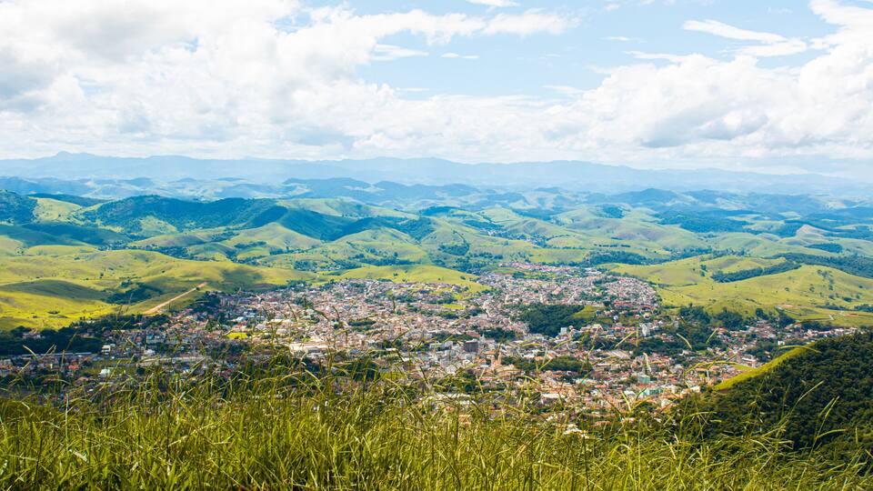 A panoramic view of a town nestled in rolling green hills under a partly cloudy sky.