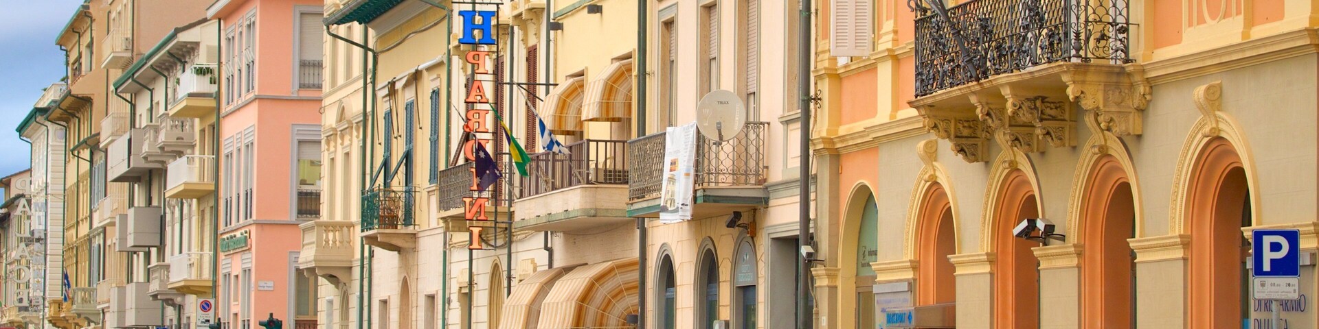 A street lined with parked cars and colorful buildings with balconies and signs.