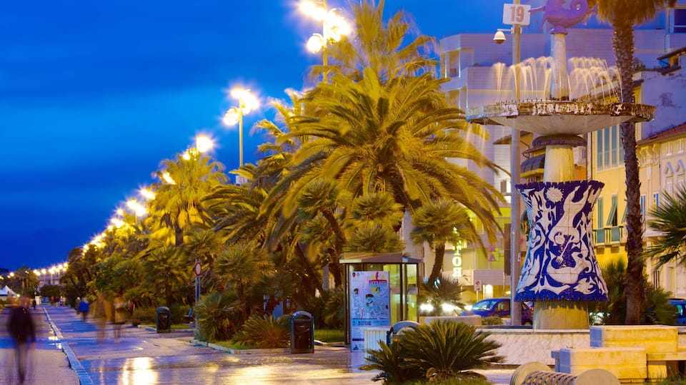 A nighttime street lined with palm trees and illuminated by street lamps.