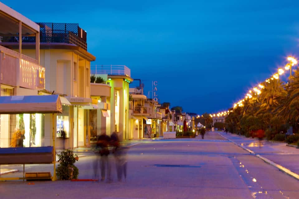A street lined with buildings at dusk, featuring illuminated signs and a palm tree-lined pathway.
