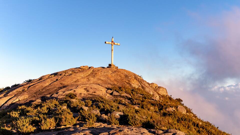 A cross on a hilltop with rocky terrain and sparse vegetation.