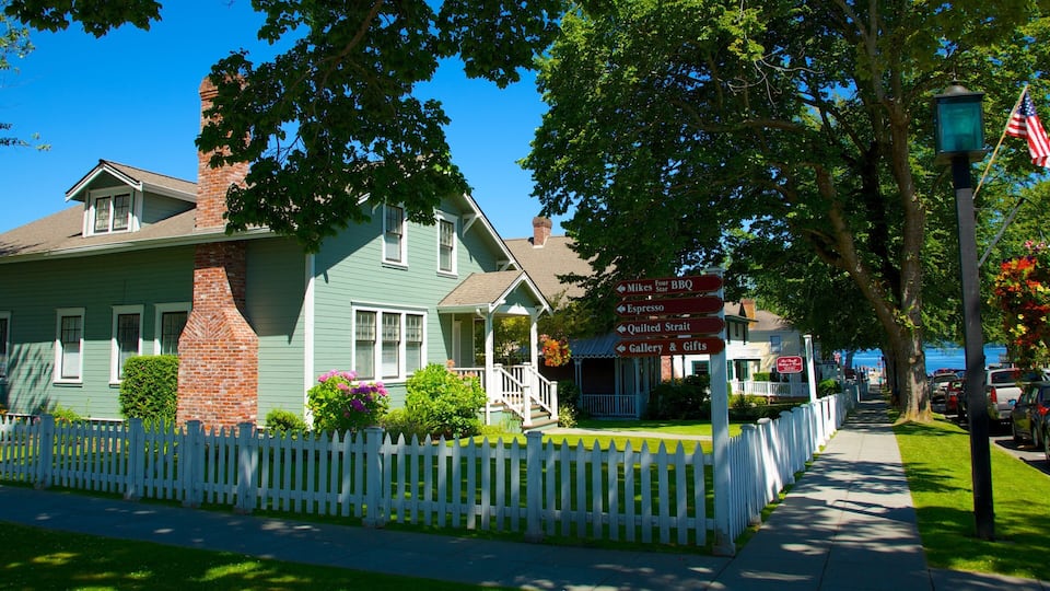 A green house with a white picket fence, a signpost with directions to local businesses, and a view of the street.
