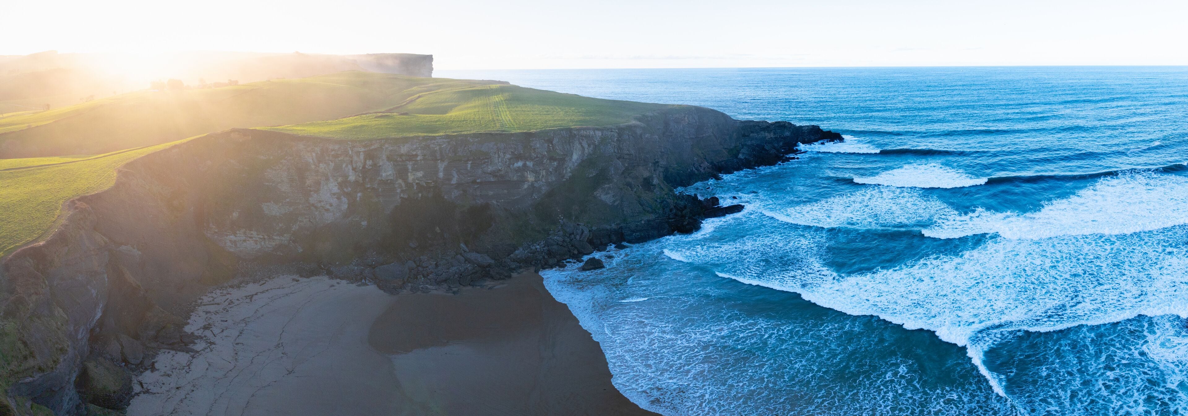 A coastal landscape with cliffs, a beach, and the ocean.