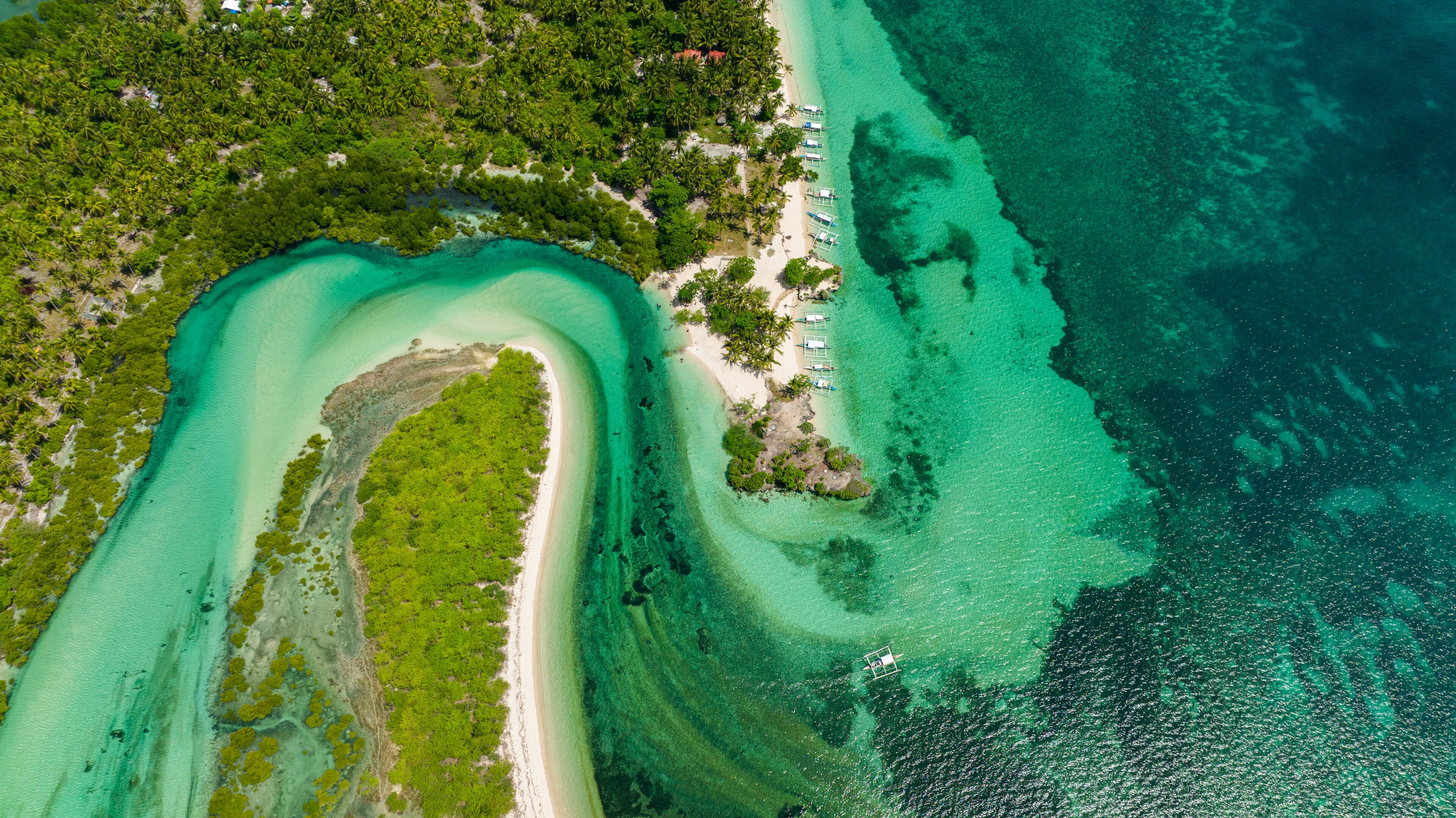 An aerial view of a tropical island with clear turquoise waters, a sandy beach, and dense green vegetation.