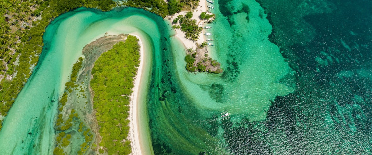 An aerial view of a tropical island with clear turquoise waters, a sandy beach, and dense green vegetation.