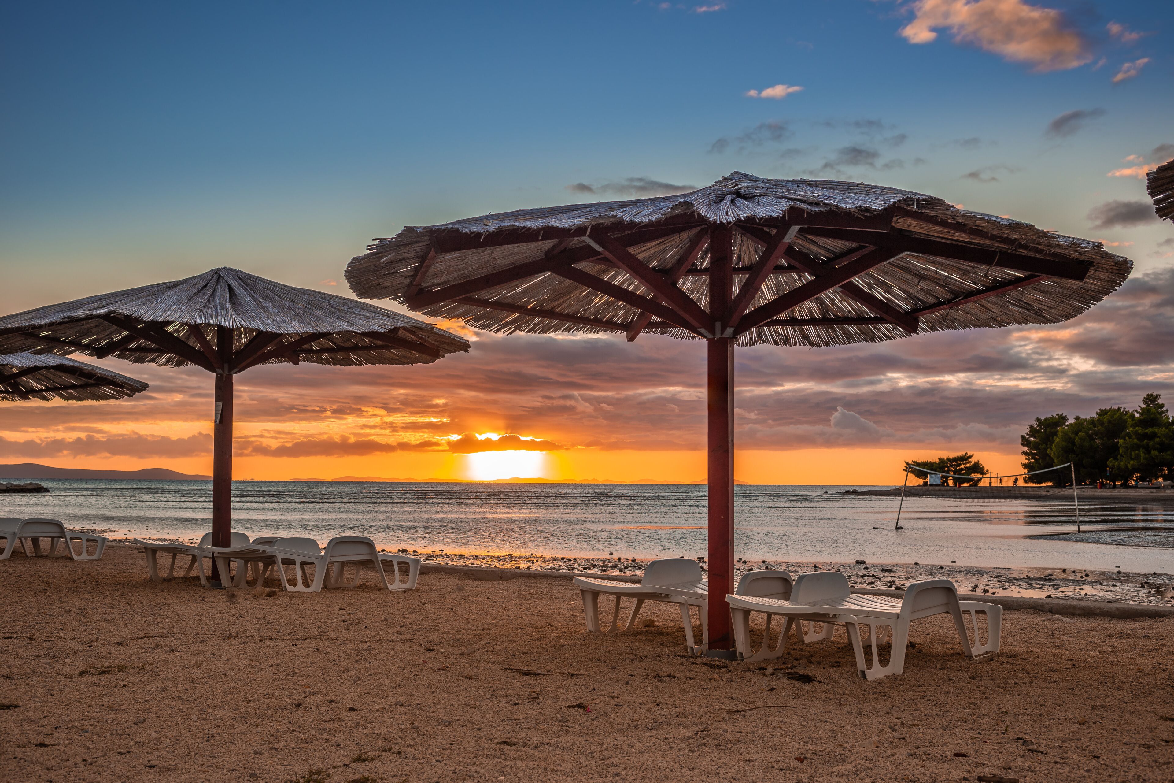 A beach with thatched umbrellas and white plastic chairs.
