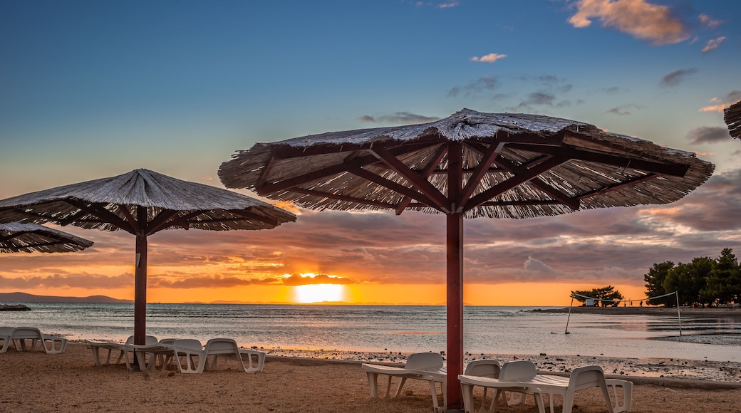 A beach with thatched umbrellas and white plastic chairs.