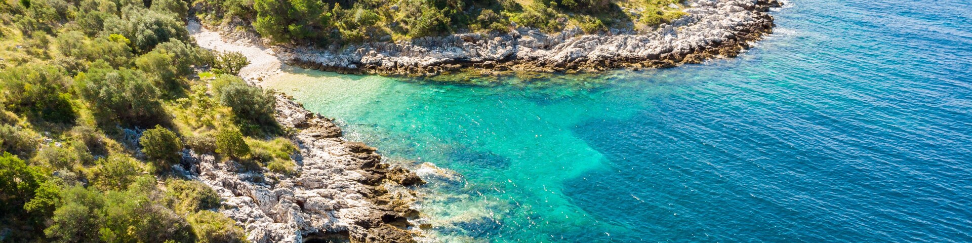 Paisagem costeira com costas rochosas, águas turquesa cristalinas e vegetação verde densa.