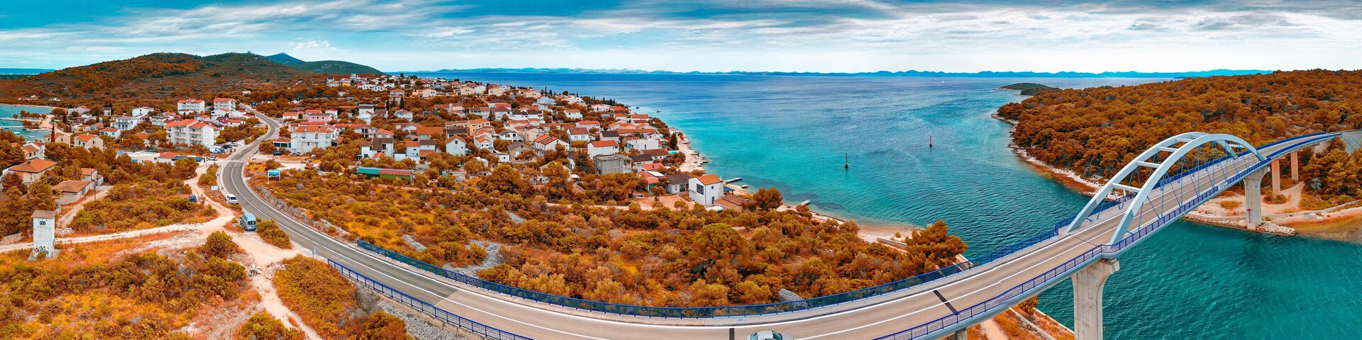 A coastal town with a bridge over water, surrounded by autumn foliage.