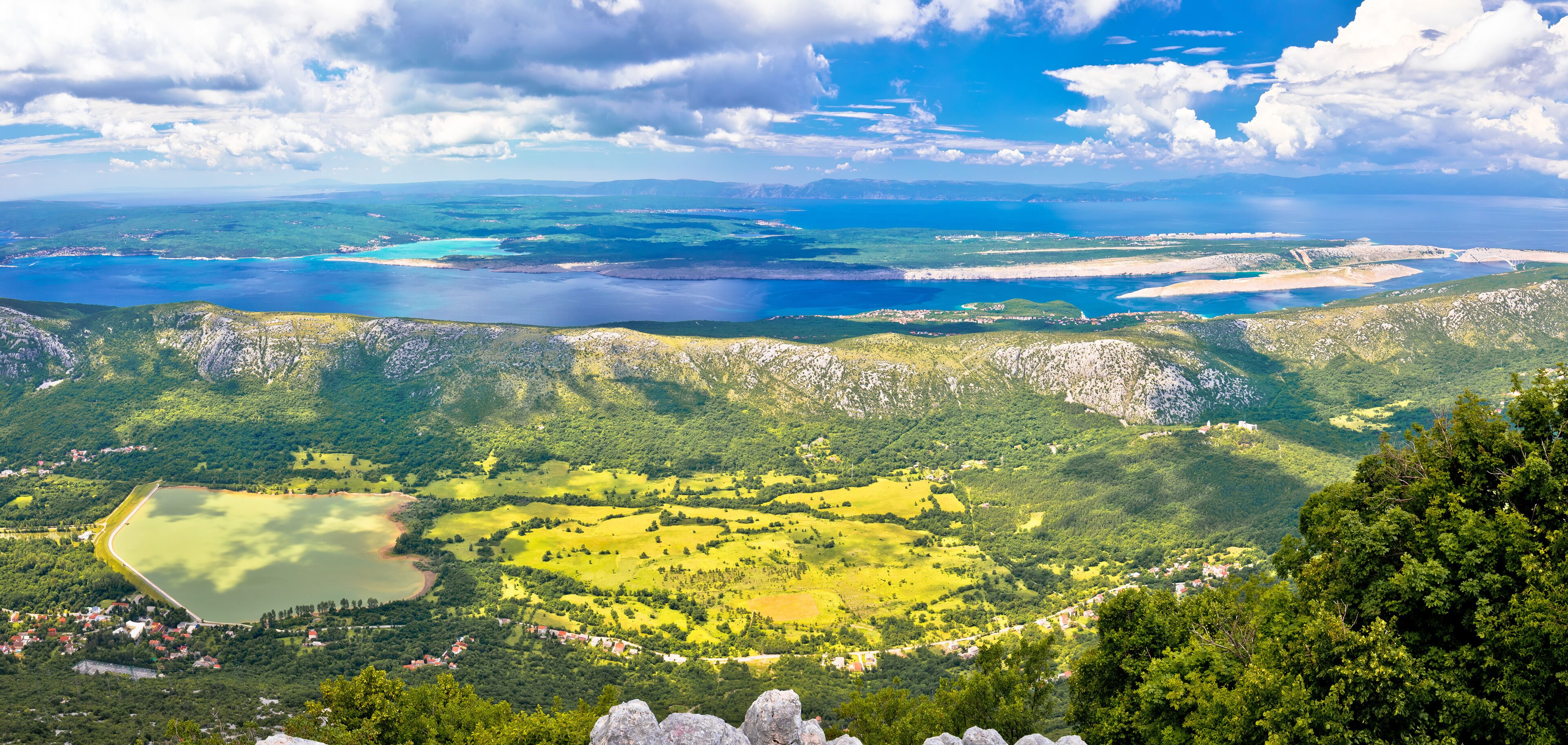 A coastal landscape with a large body of water, green hills, and scattered buildings.