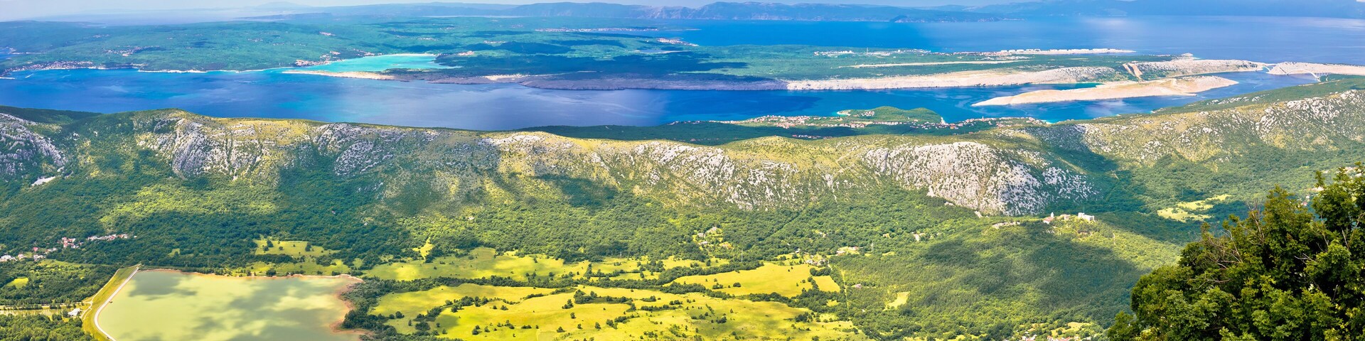 A coastal landscape with a large body of water, green hills, and scattered buildings.