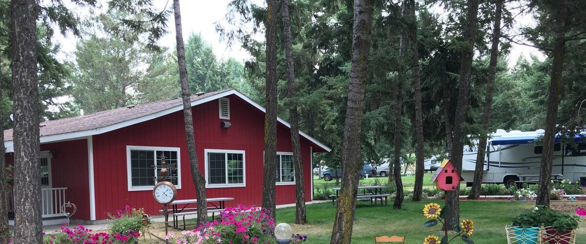 A red house with a porch, surrounded by trees and potted plants.