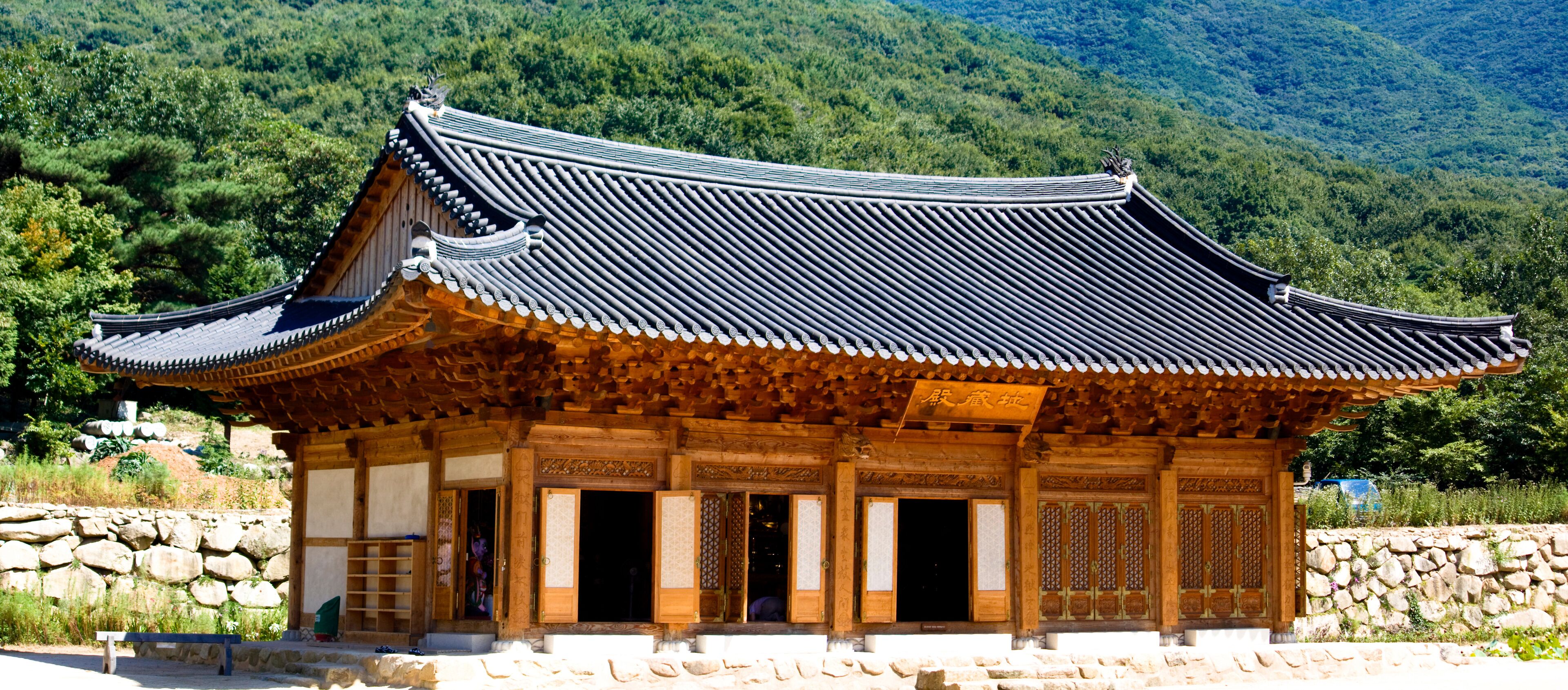 A traditional Korean building with a curved roof and wooden architecture, surrounded by lush greenery and mountains.