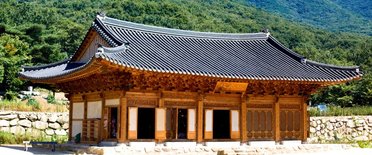 A traditional Korean building with a curved roof and wooden architecture, surrounded by lush greenery and mountains.