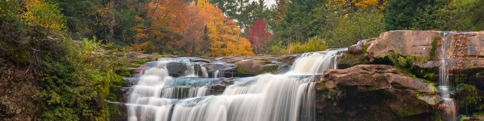 O Kun-de-Kun Falls nestled against an autumn-colored forest, on the Baltimore River, near Bruce Crossing, Michigan.