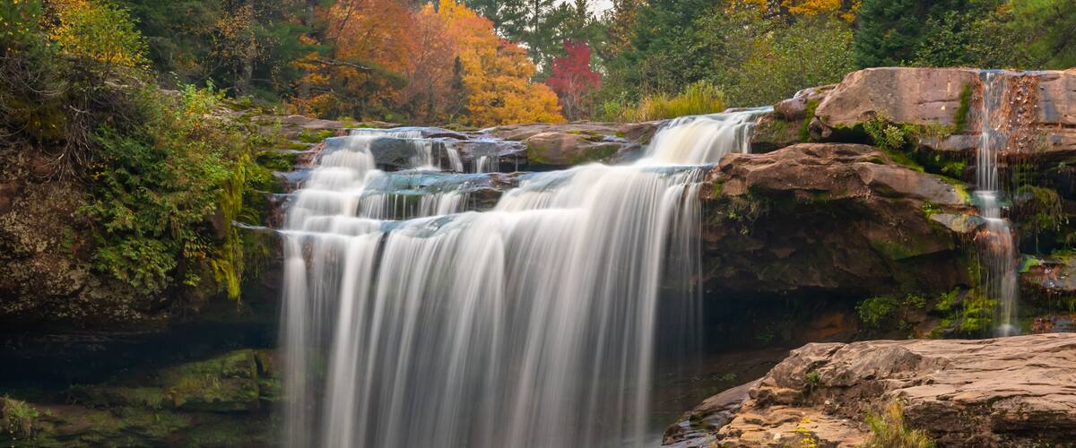 A waterfall cascading over rocks in a forested area with autumn foliage.