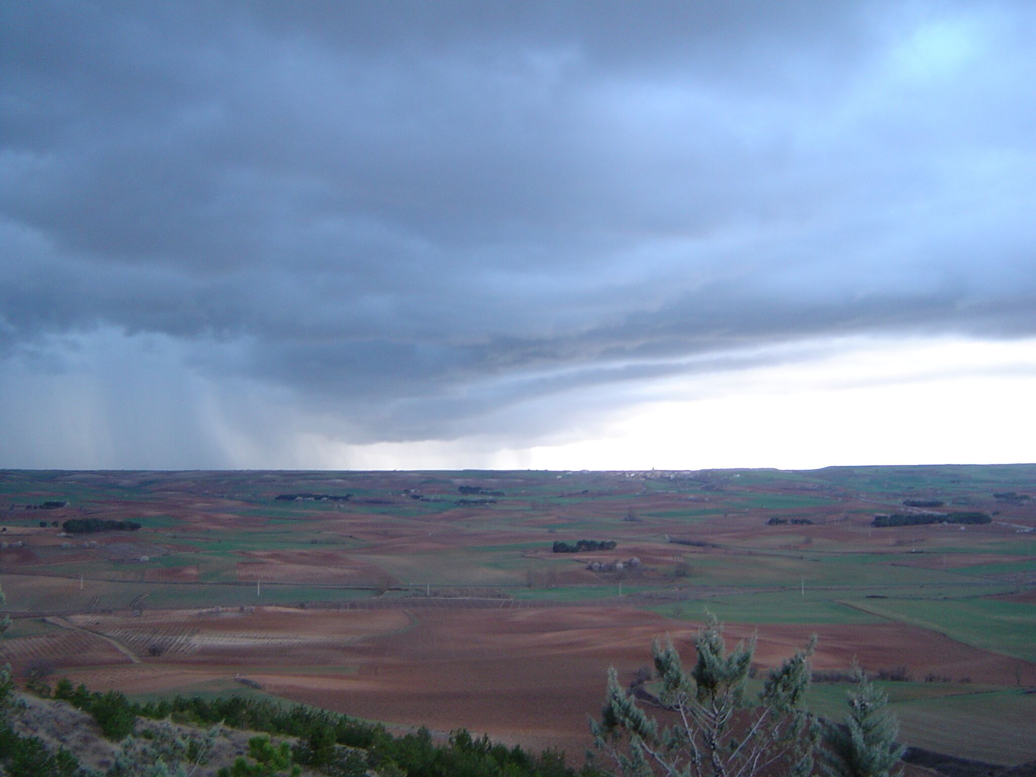 A vast landscape with rolling hills and fields under a cloudy sky.