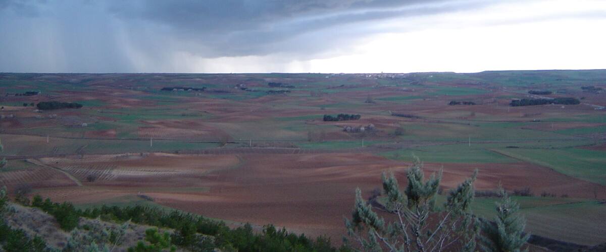 A vast landscape with rolling hills and fields under a cloudy sky.