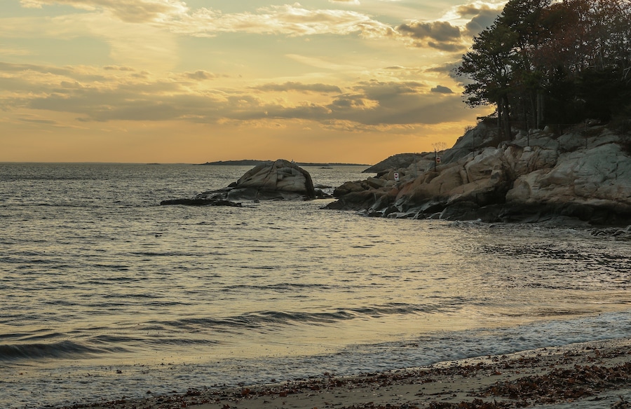 Paisagem costeira com afloramentos rochosos e mar calmo ao pôr do sol.