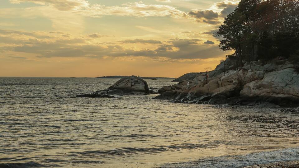 A coastal landscape with rocky outcrops and calm sea during sunset.