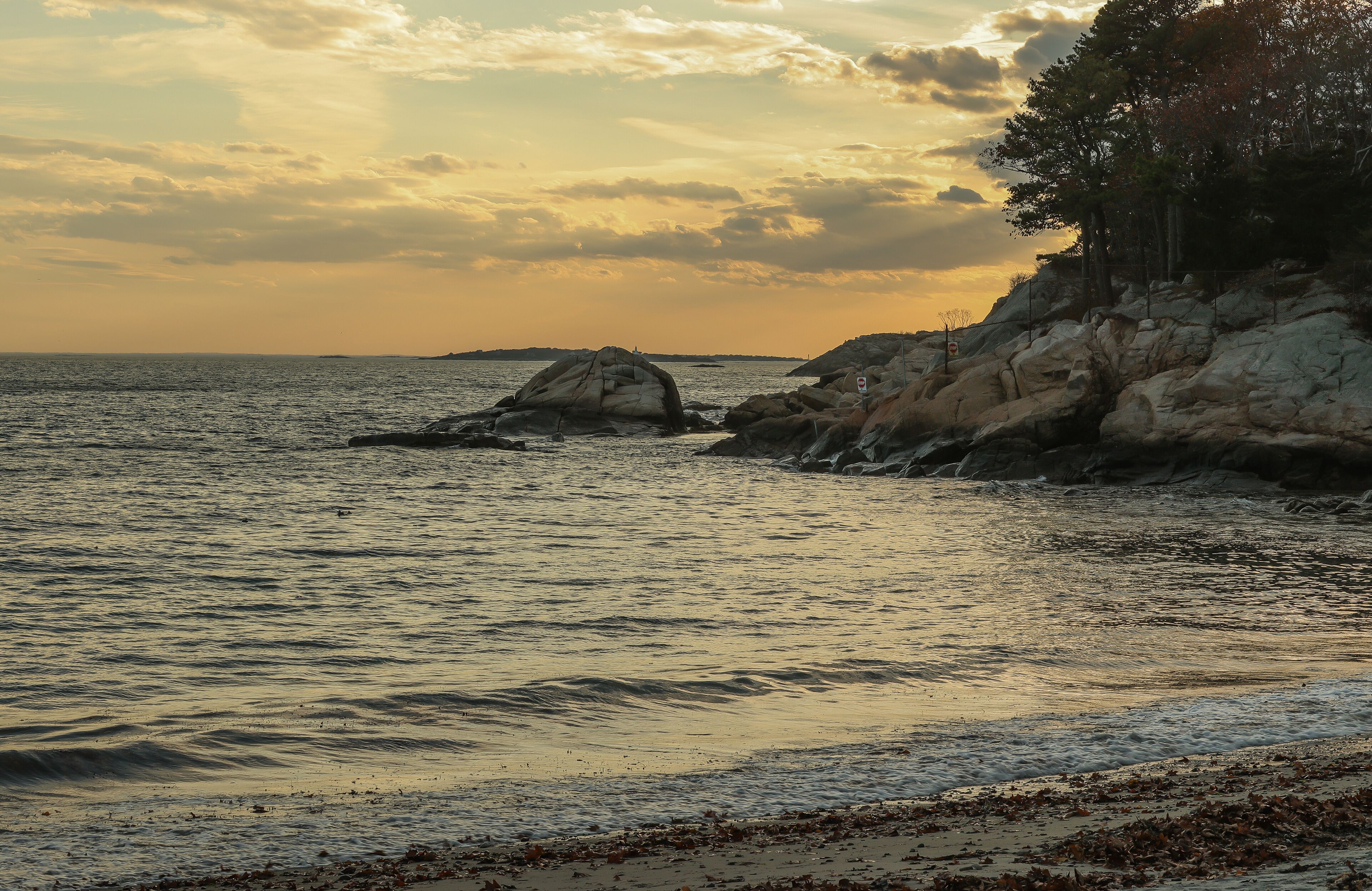 A coastal landscape with rocky outcrops and calm sea during sunset.