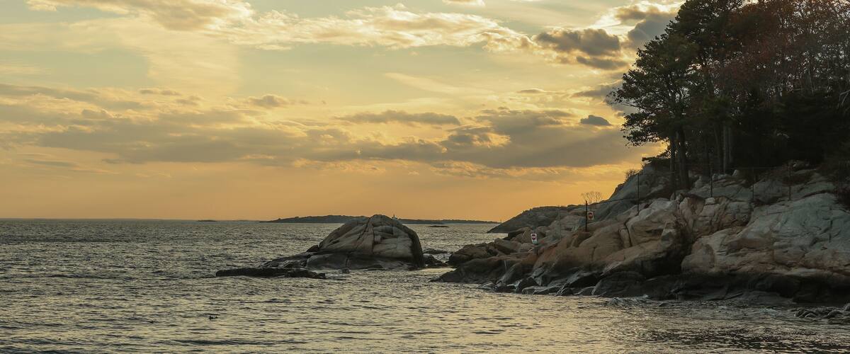 A coastal landscape with rocky outcrops and calm sea during sunset.