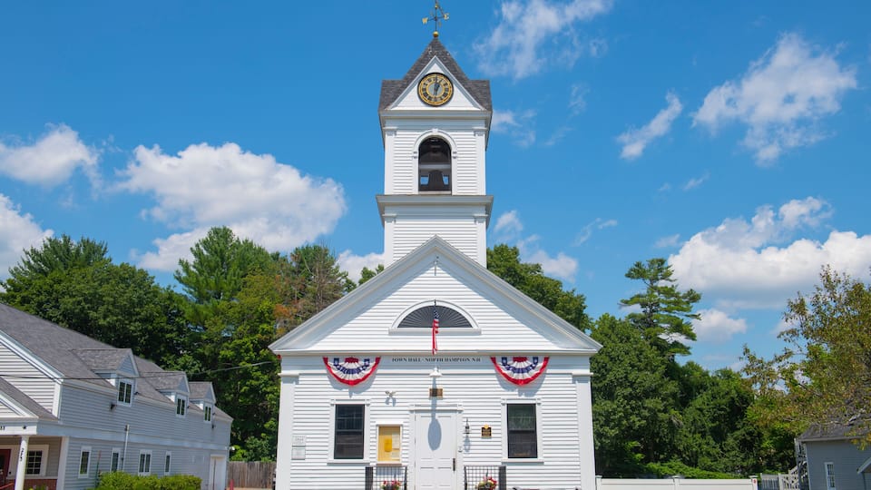A white church with a clock tower, surrounded by trees and a clear blue sky.