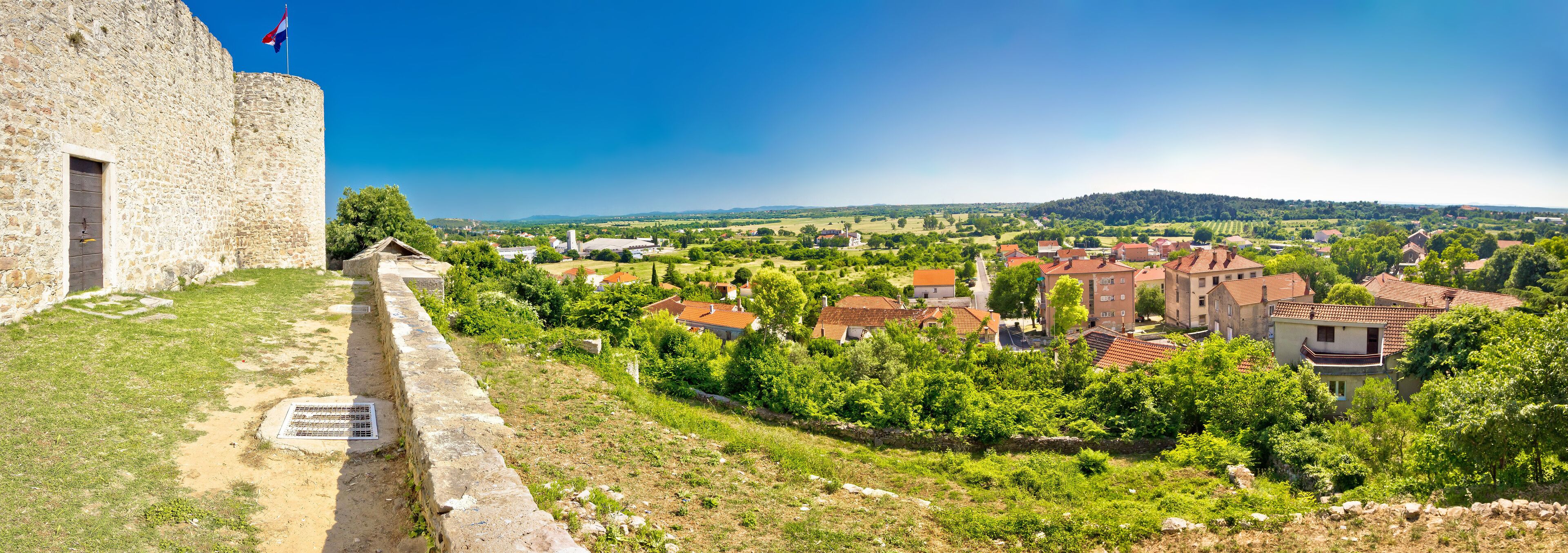 A stone fort with a flag, surrounded by a rural landscape with houses and trees.