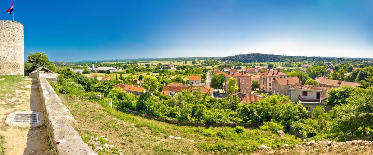 A stone fort with a flag, surrounded by a rural landscape with houses and trees.
