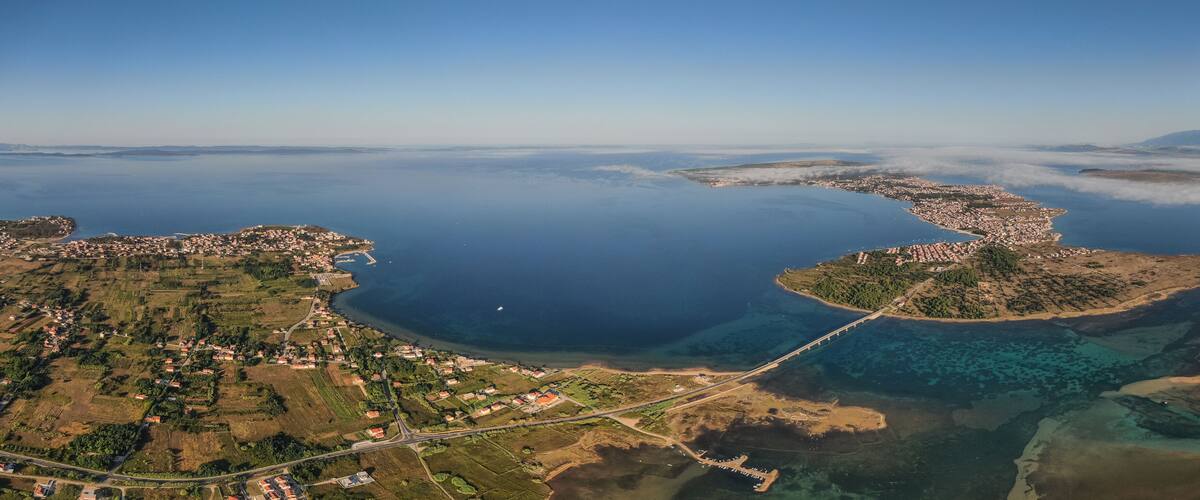 An aerial view of a coastal town with a bridge, clear blue waters, and surrounding greenery.