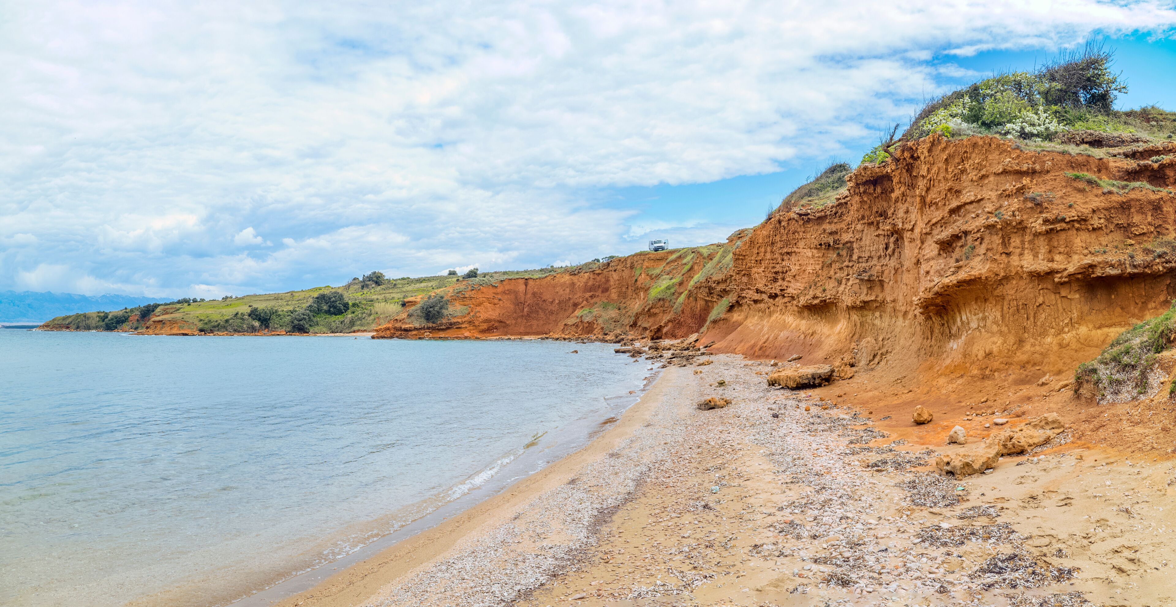 Duboka Draga Beach, Vir Island, Croatia: Red cliffs meet the sea under a cloudy sky