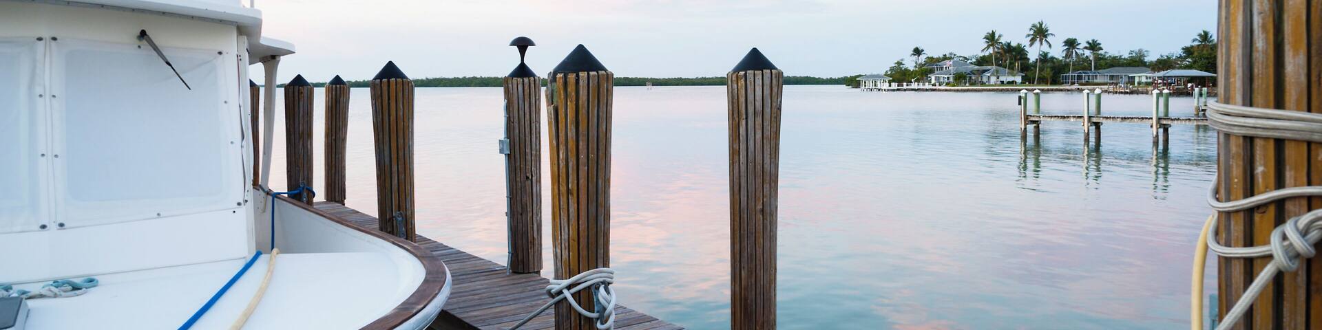 A boat docked at a wooden pier with a calm water body and distant palm trees.