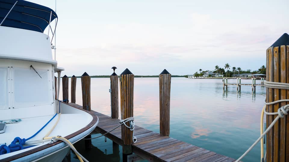 The sun is setting over the ocean with a anchored boat on the pier in Naples, Florida.
