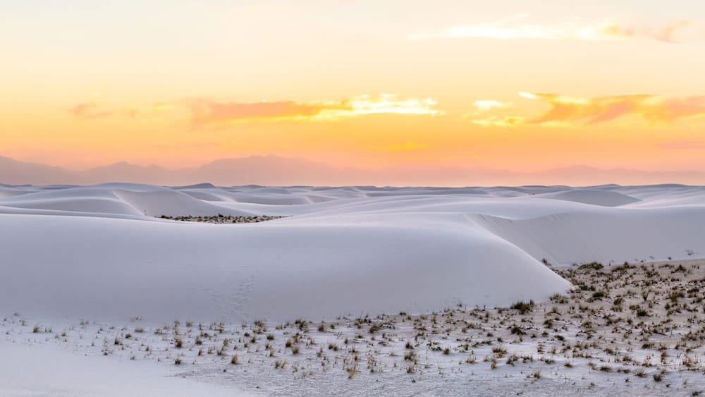 Panorama panoramic view of Organ mountains silhouette at White sands national park monument sand dunes and plants in New Mexico at colorful orange yellow sunset
