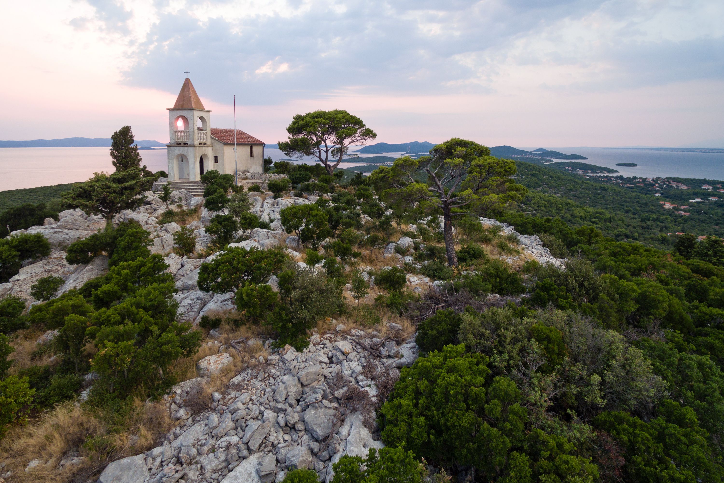 Igreja no topo de uma colina, com vista para o mar e montanhas ao longe.
