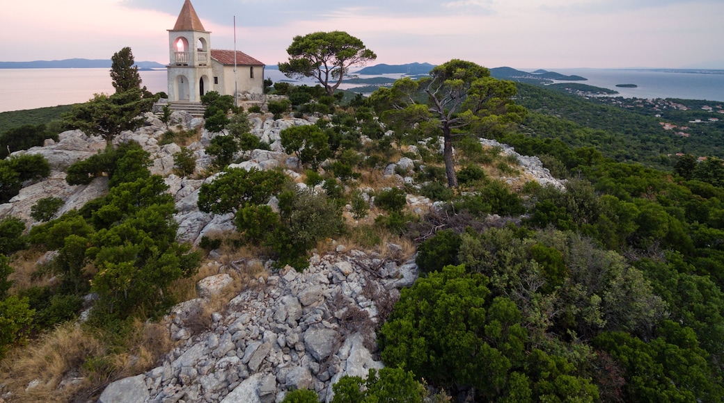 Igreja no topo de uma colina, com vista para o mar e montanhas ao longe.