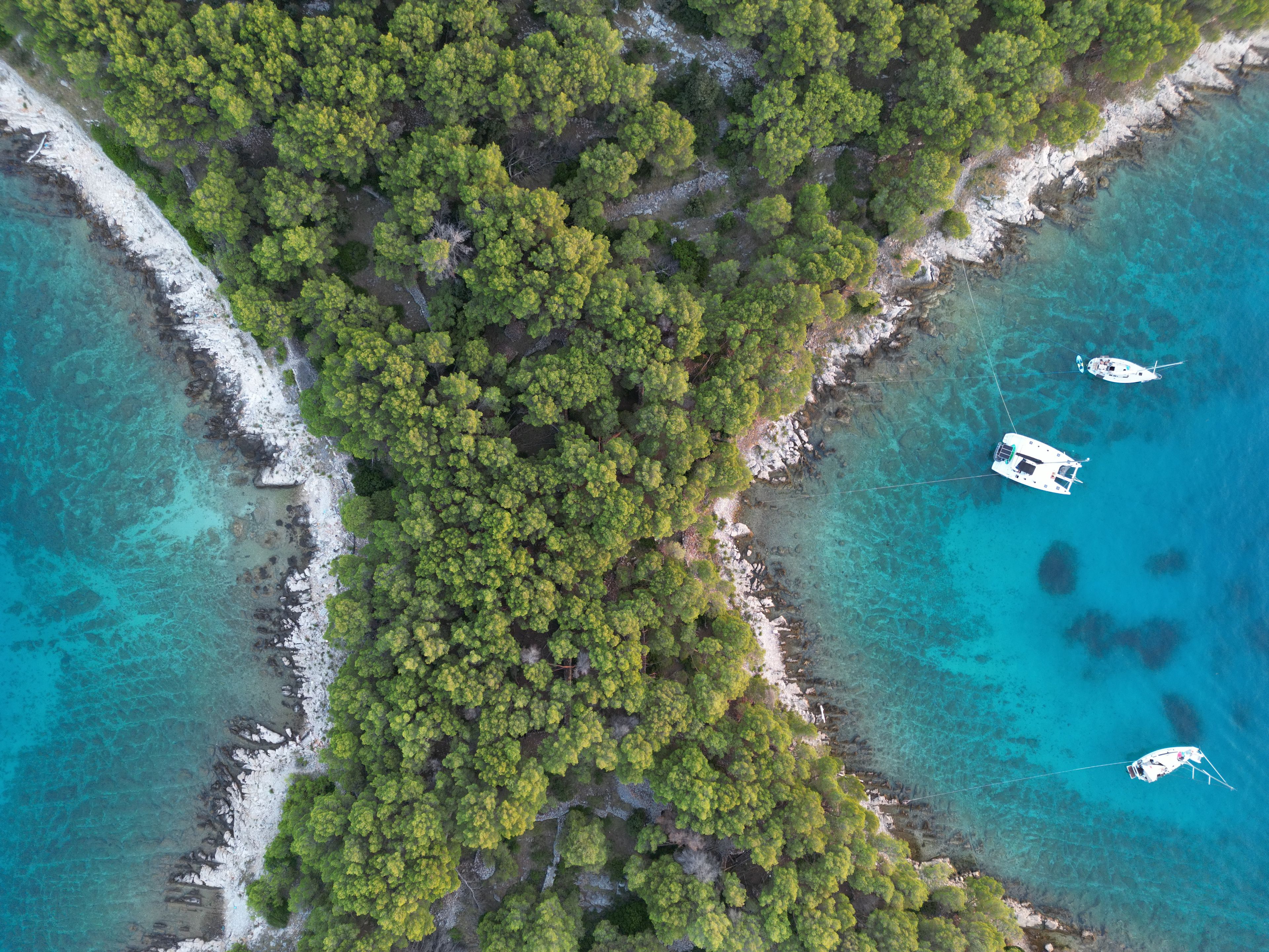Vista aérea de uma área costeira com vegetação verde exuberante, águas turquesas cristalinas e alguns barcos ancorados perto da costa.