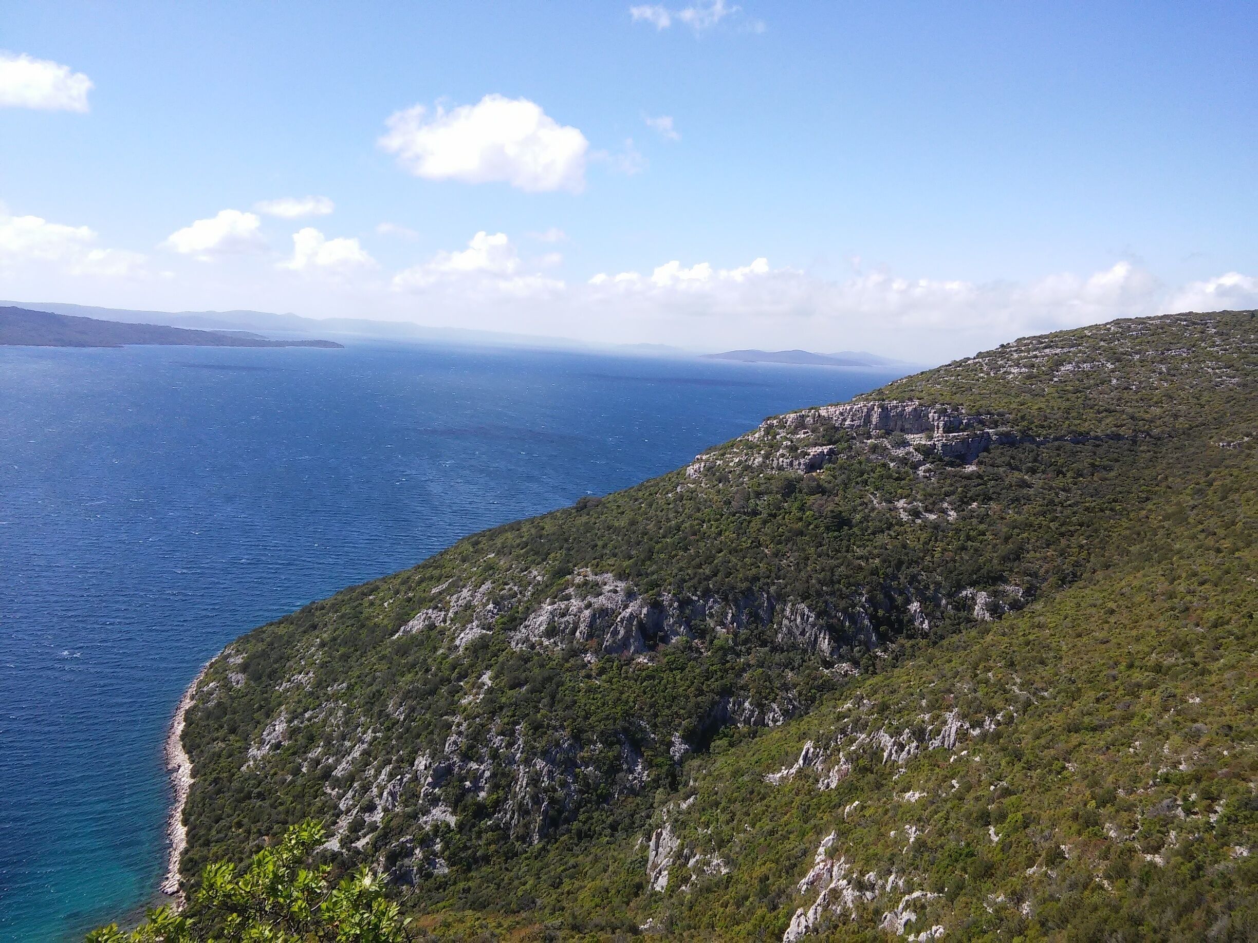 A coastal landscape with a clear blue sea, green hills, and rocky cliffs.