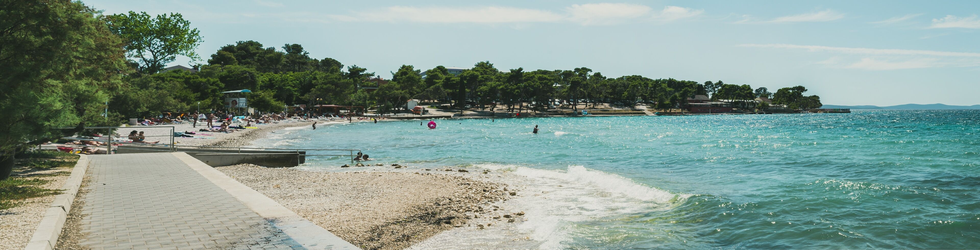 A beach with pebbles, a pathway, and a row of trees.