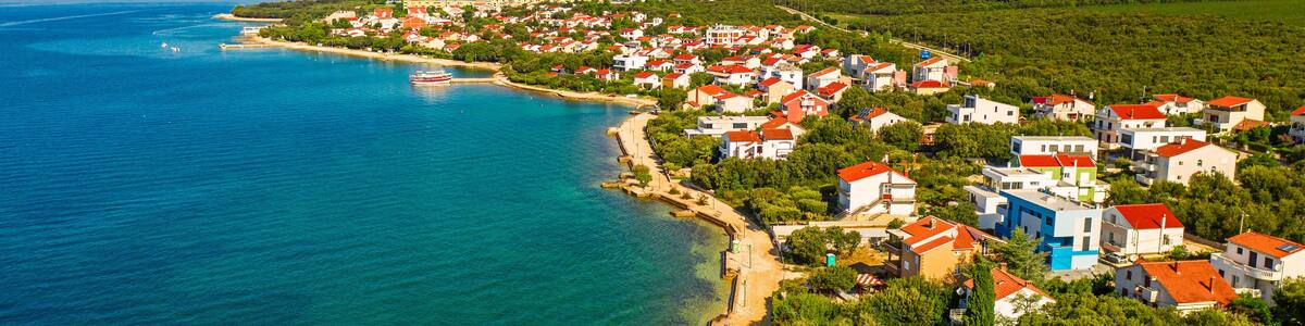 Une ville côtière avec une plage, des maisons aux toits rouges et une mer d’un bleu limpide.