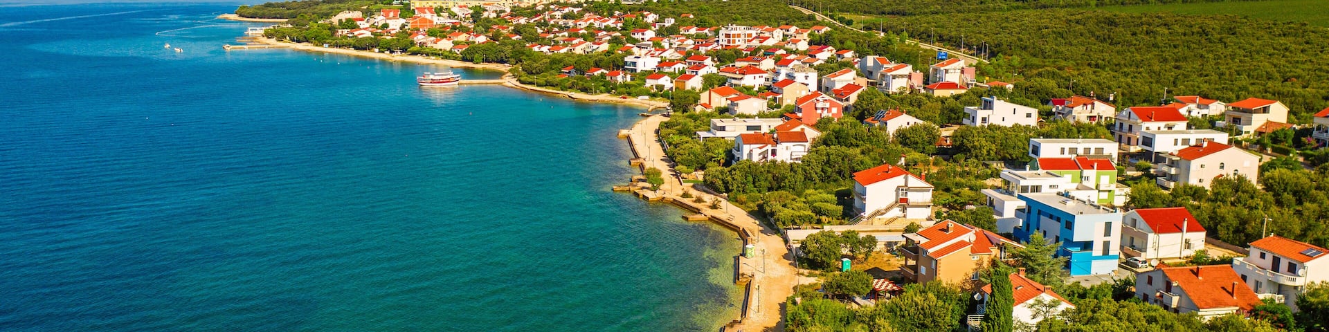 A coastal town with a beach, houses with red roofs, and a clear blue sea.