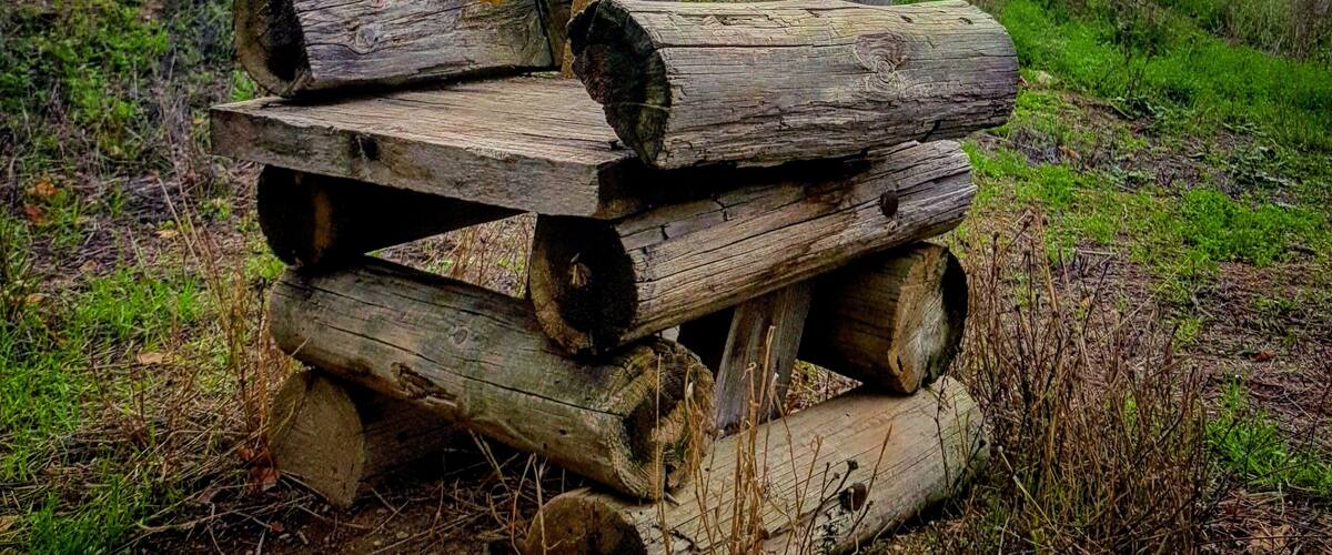 A rustic wooden bench made of logs in a grassy field with a cloudy sky.