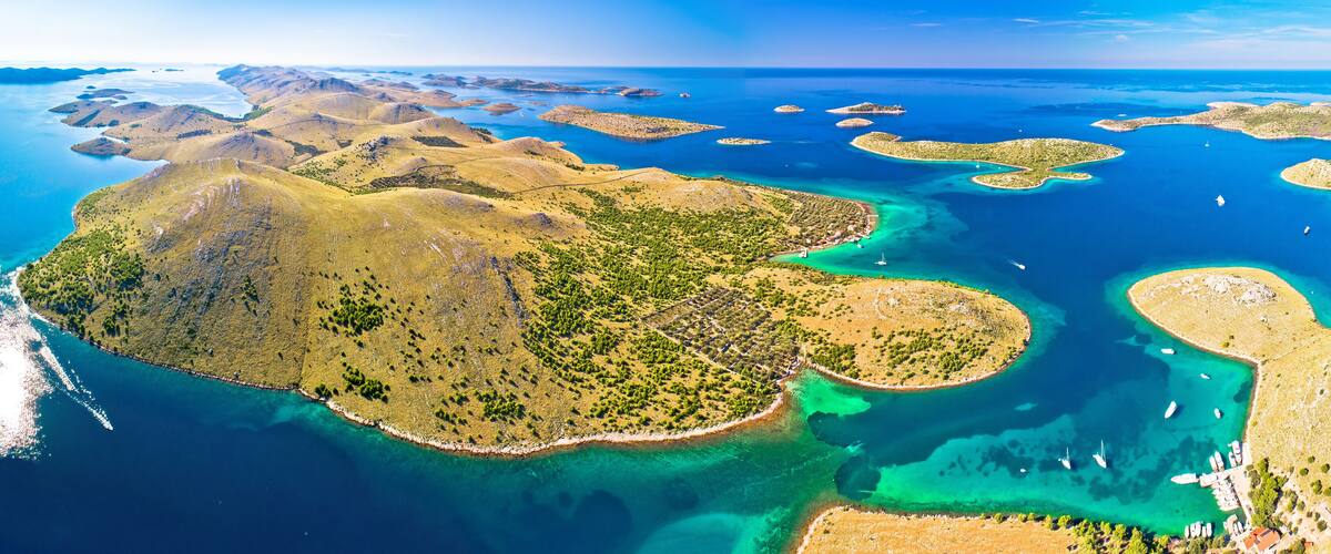 An aerial view of a coastal landscape with multiple islands, clear blue waters, and a mix of green vegetation and rocky terrain.